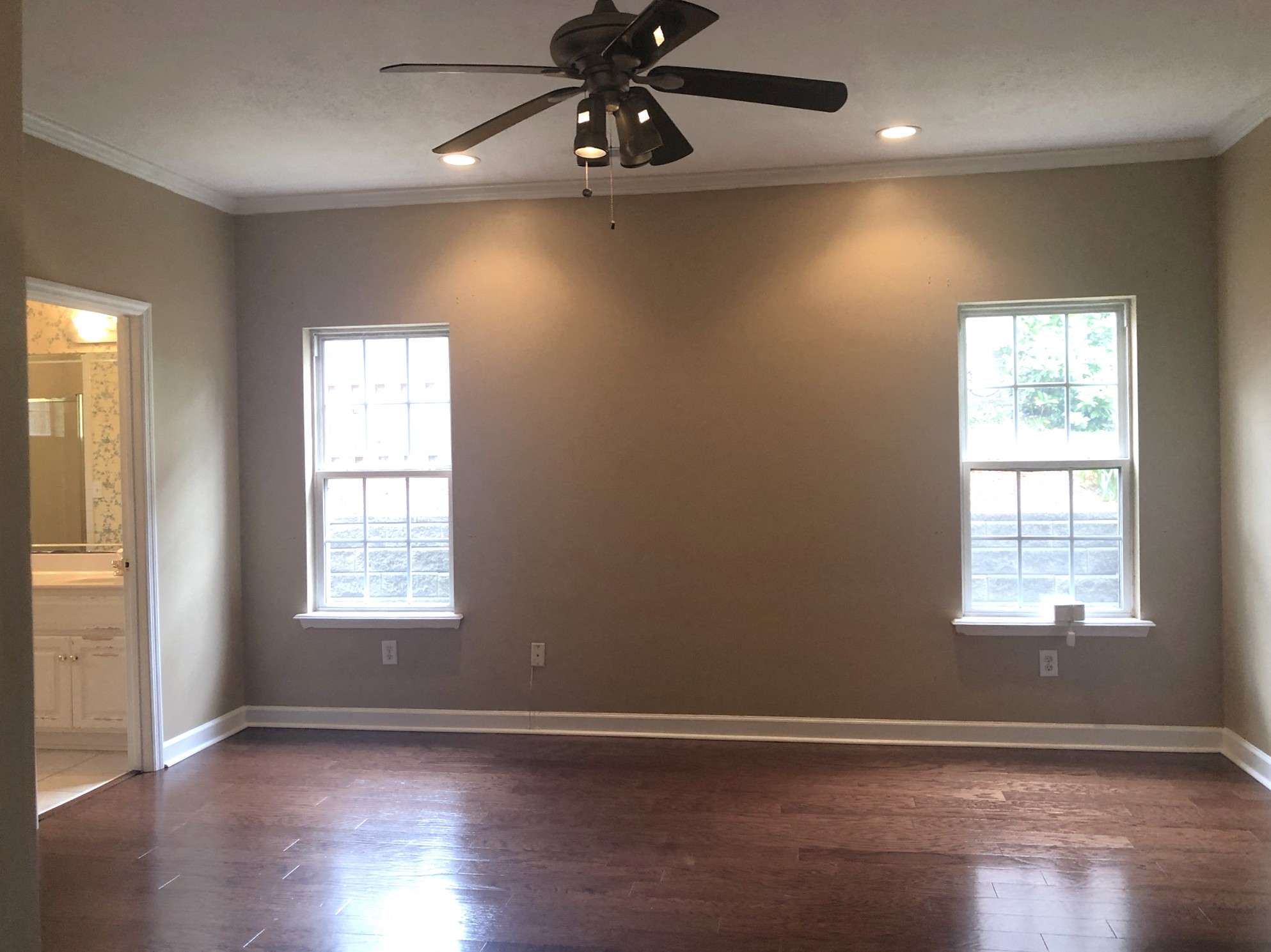 an empty living room with a ceiling fan and two windows